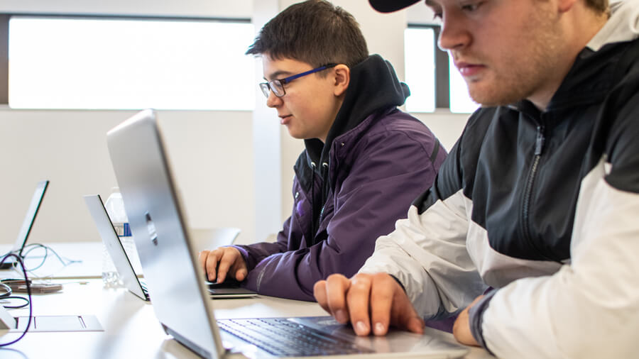 Two students sit at a lab table in Helmke Library while using their laptops.