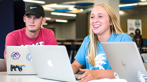 Students sit around a table with their laptops out, talking about taking summer classes.
