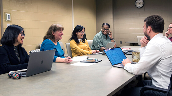Faculty gather in a boardroom for a meeting.