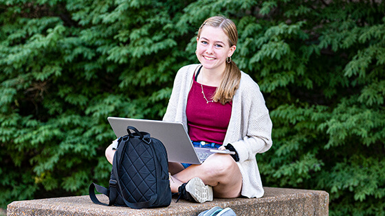 A PFW student works on a laptop outside.