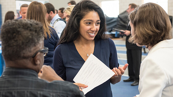 A student smiles as she discusses internships with potential employers at a career fair.