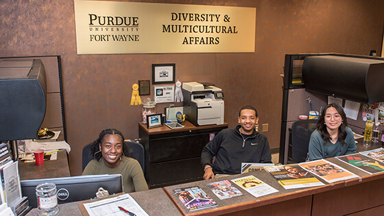 The Office of Diversity and Multicultural Affairs front desk staff smile for a group photo at their workstations.