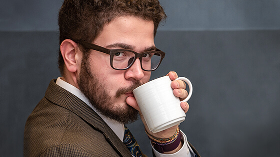 A student drinks from a mug of coffee.
