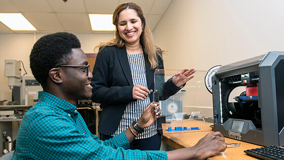 A student works with a Dremel machine while an instructor helps.