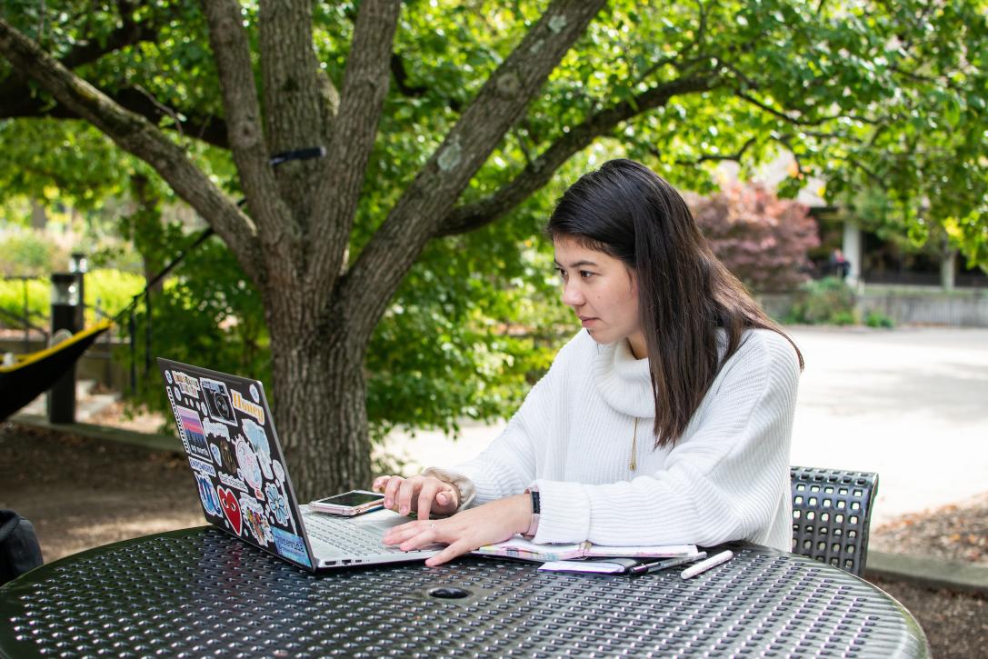 Student outdoors writing on a laptop.