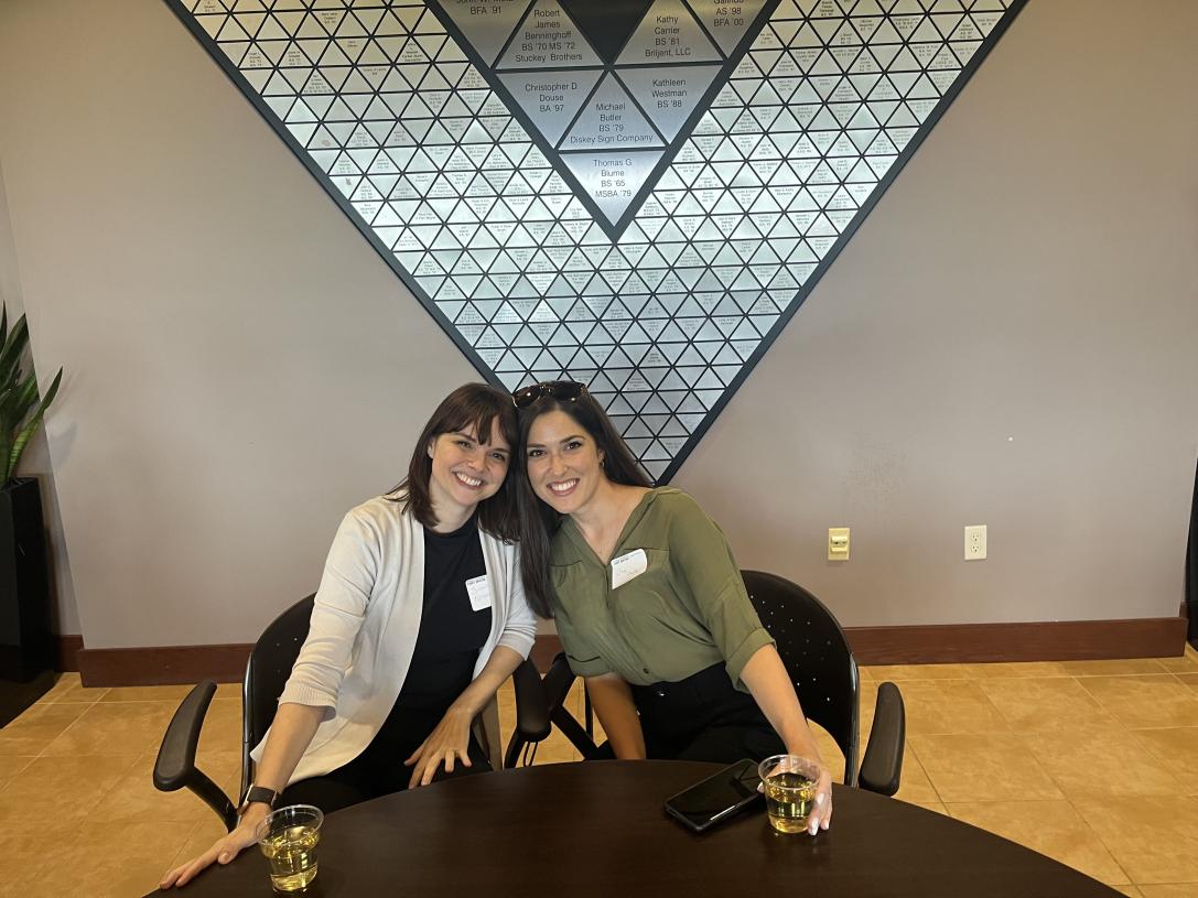 Two alumni at our annual Oktoberfest smiling and leaning towards each other