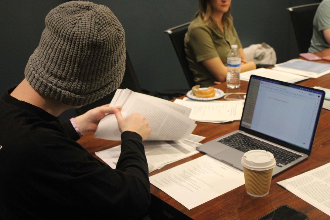 Looking over students right shoulder while the student looks through paperwork with laptop open.