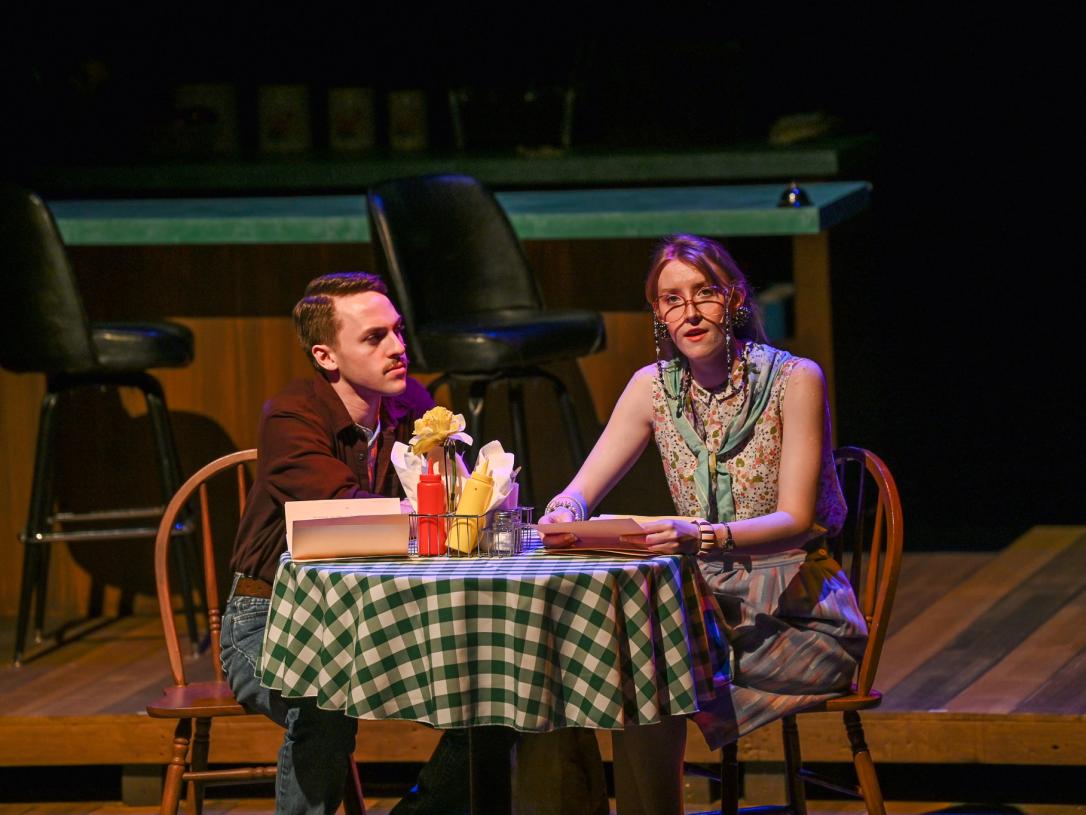 Man and woman actor sitting on stage at a diner set
