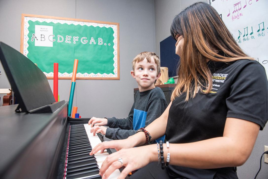 A music therapy student plays piano with a young student.