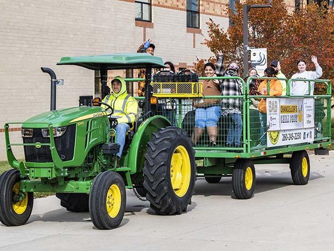 Faculty and staff are being pulled by a green John Deere tractor for a hayride