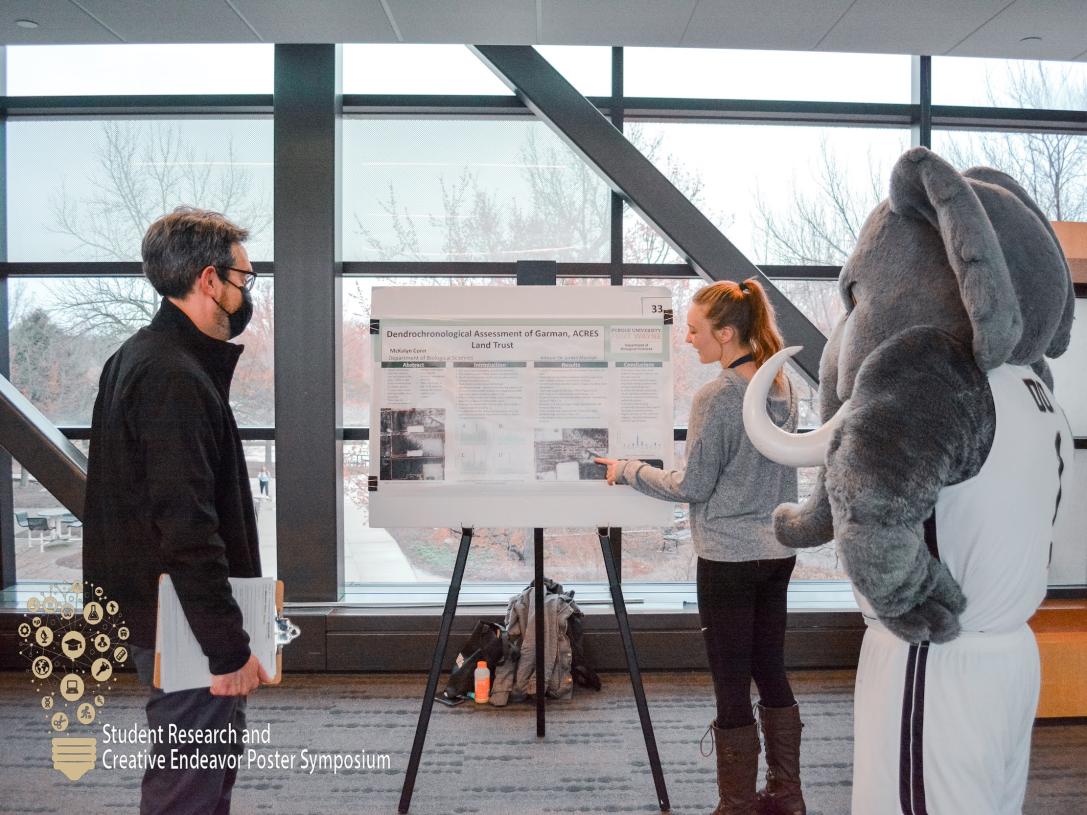 A student presents research findings to Don and a faculty member.