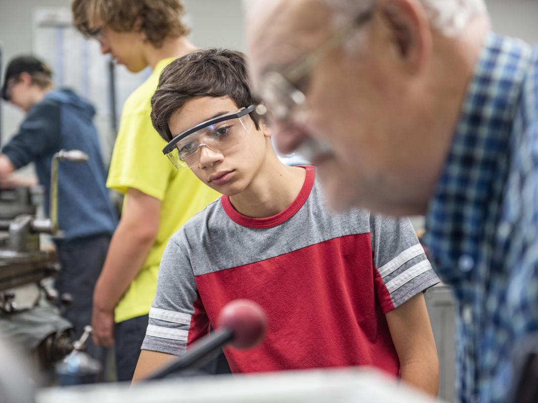A student at the machining tools in engineering summer STEM exploration camp receives instruction
