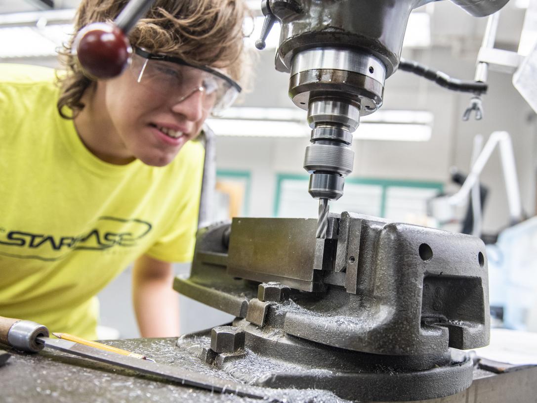 A student learning how to use a drill press