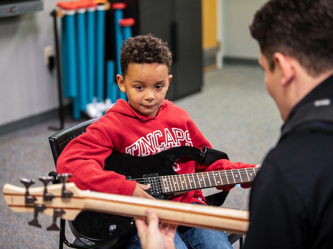 A music therapy student is playing guitar with a young boy.