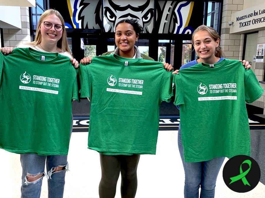 Female students holding green Mental Health Awareness Week T-shirts