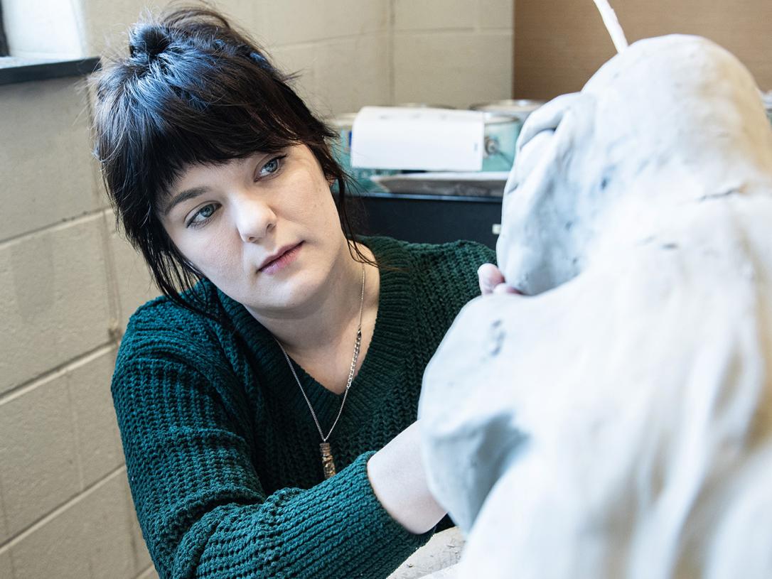 Emily Whisman is sculpting in an art studio
