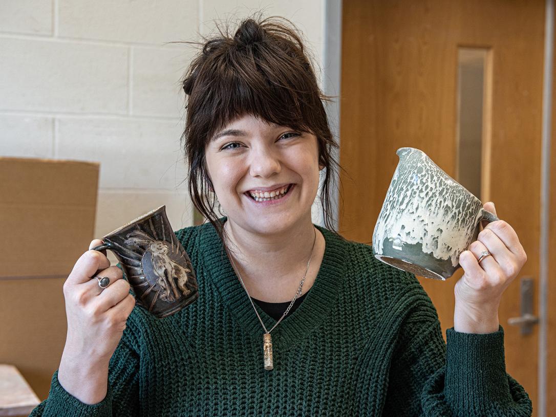Emily Whisman is holding two pottery mugs she created