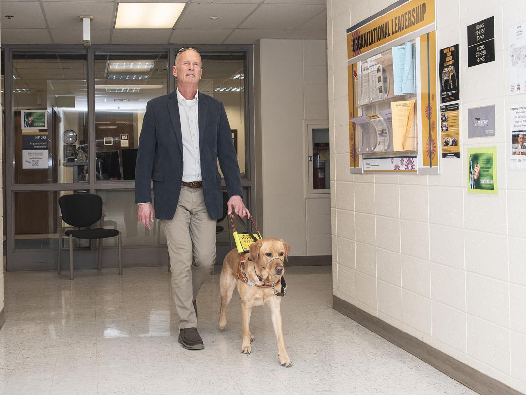Jim Platzer and his leader dog are walking through a hallway