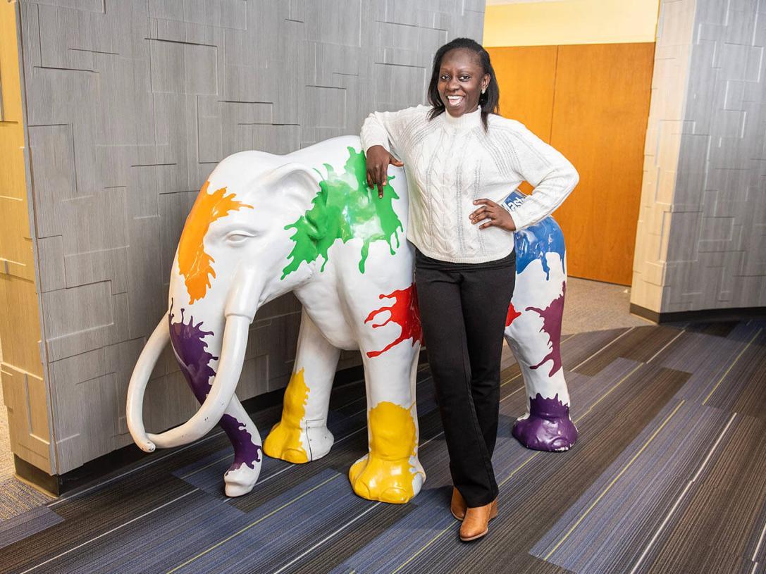 Kaliyat Gamba is standing beside a mastodon statue.