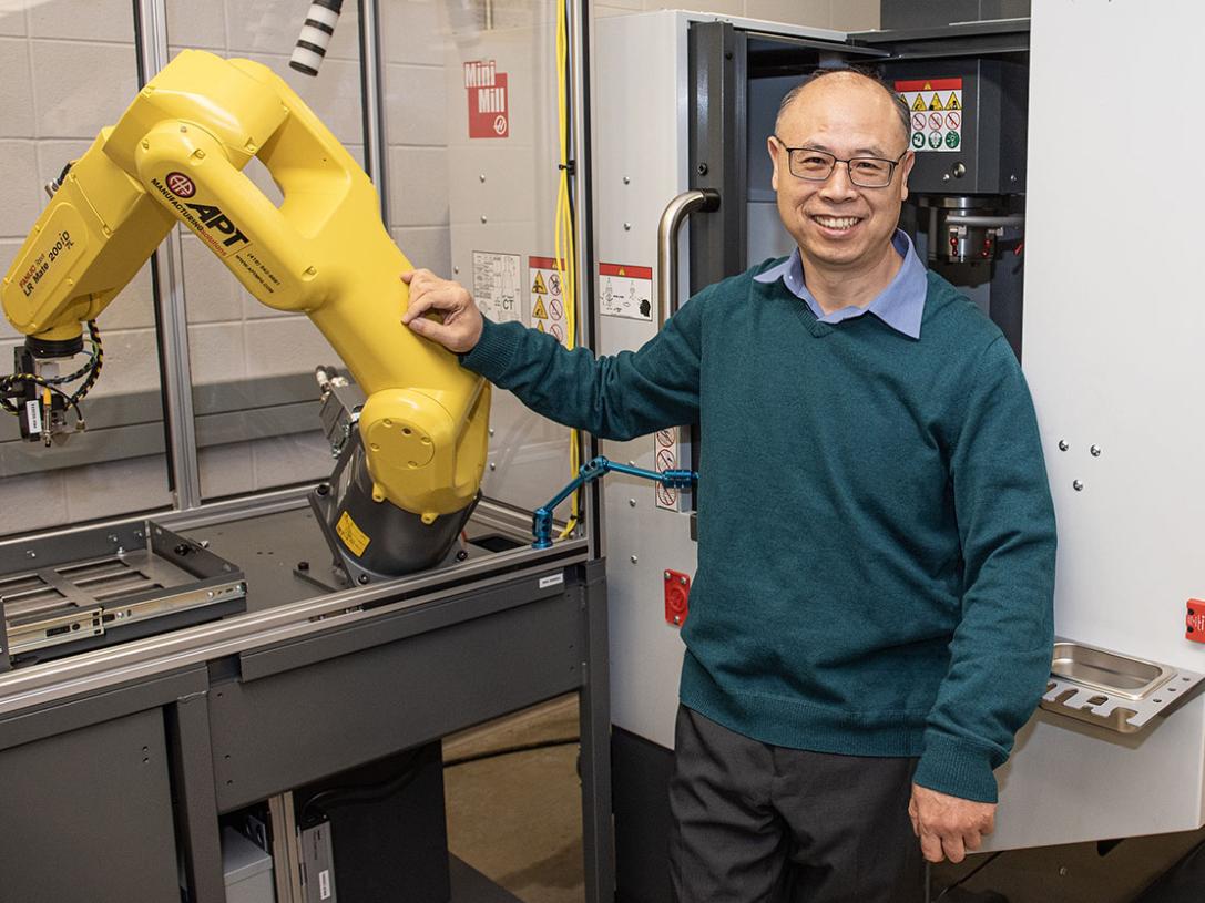 Zhuming Bi is standing next to a robotic arm