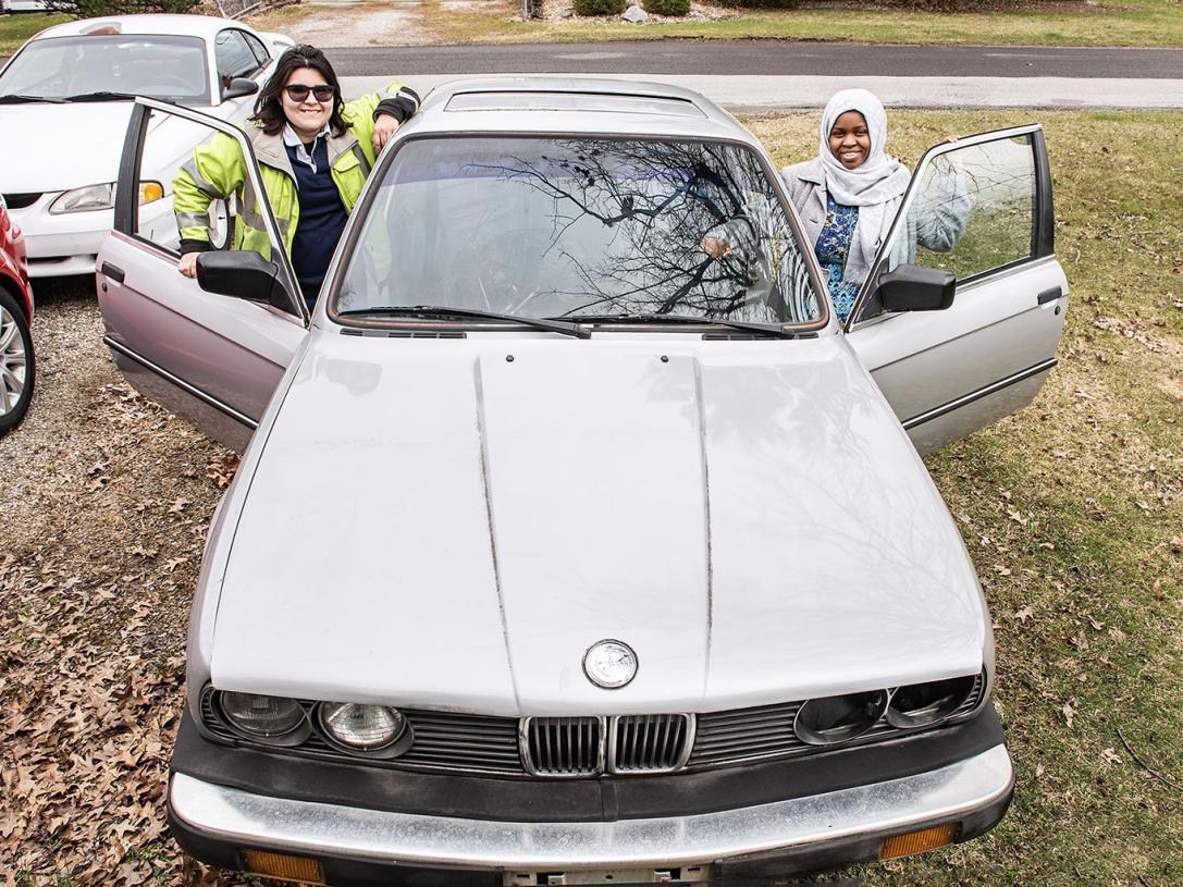 Two polytechnic students are standing beside the BMW care they're working on.