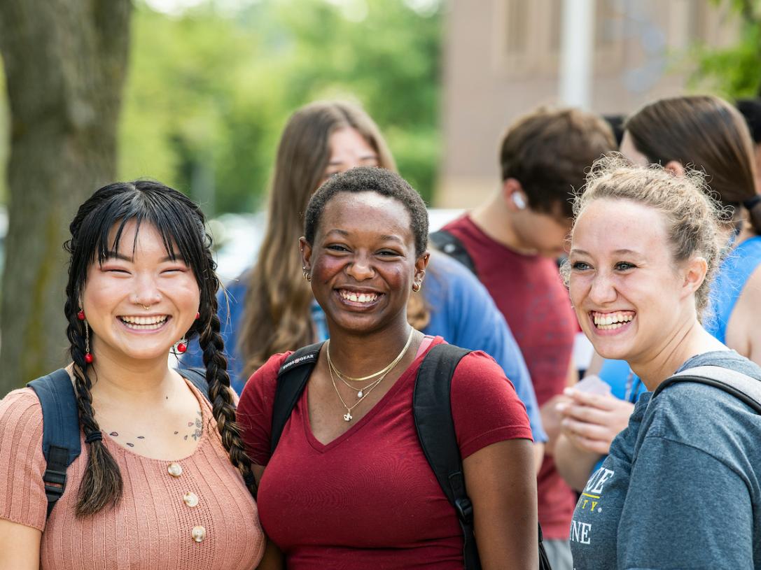 Students with backpacks on outside smiling for the camera.