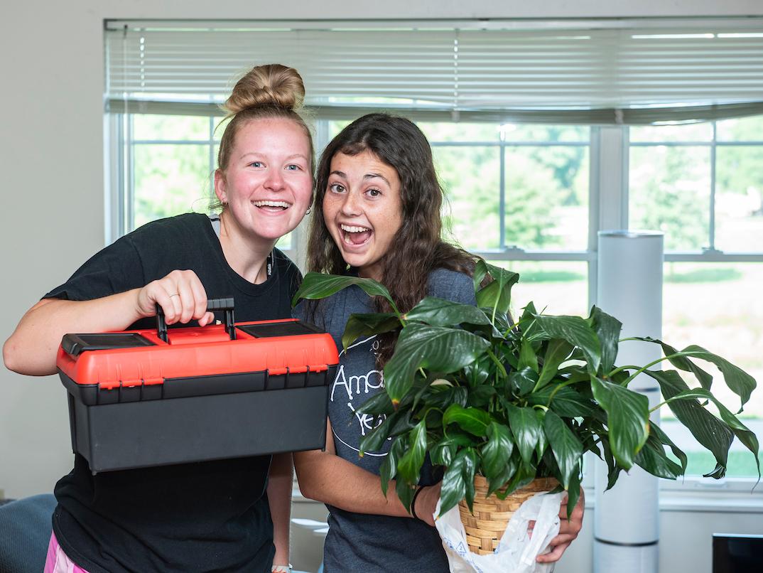 Students on move-in day holding up apartment items.