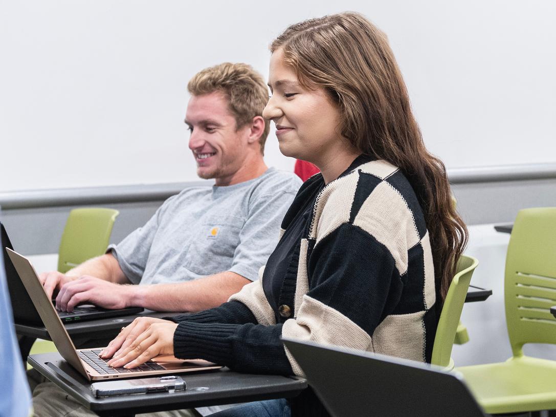 Students smile while taking notes during a class.