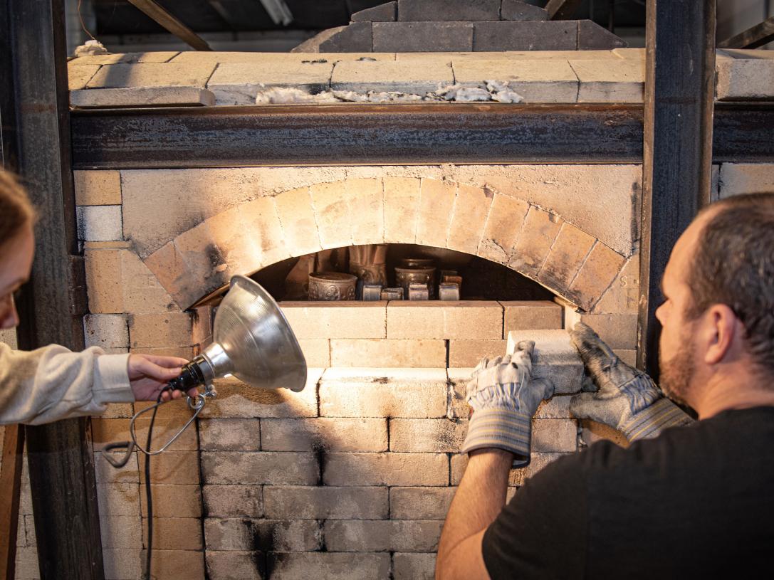 Two people are loading a wood burning kiln