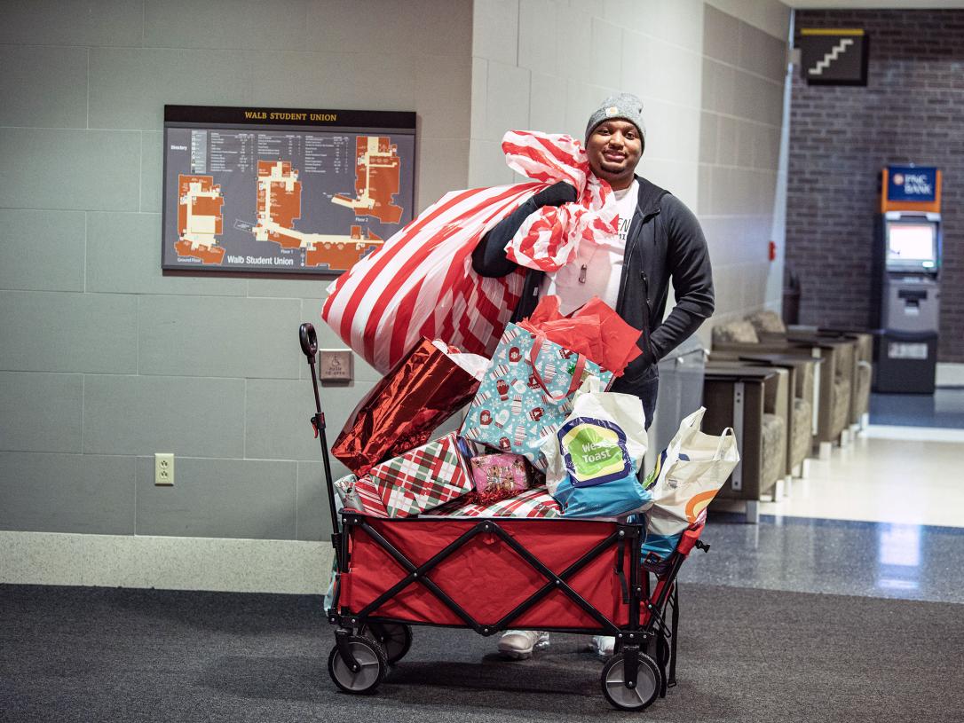 A man is standing beside a cart full of holiday gifts