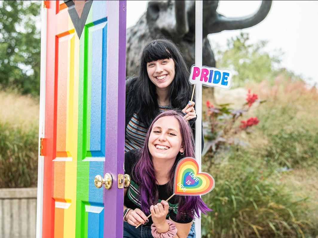 Two students posing in front of rainbow door