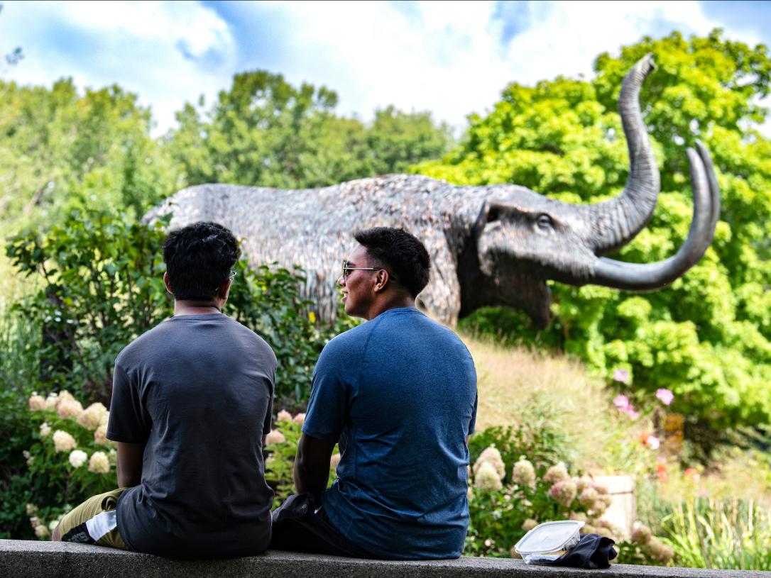 Two students site on a ledge near the Mastodon statue.
