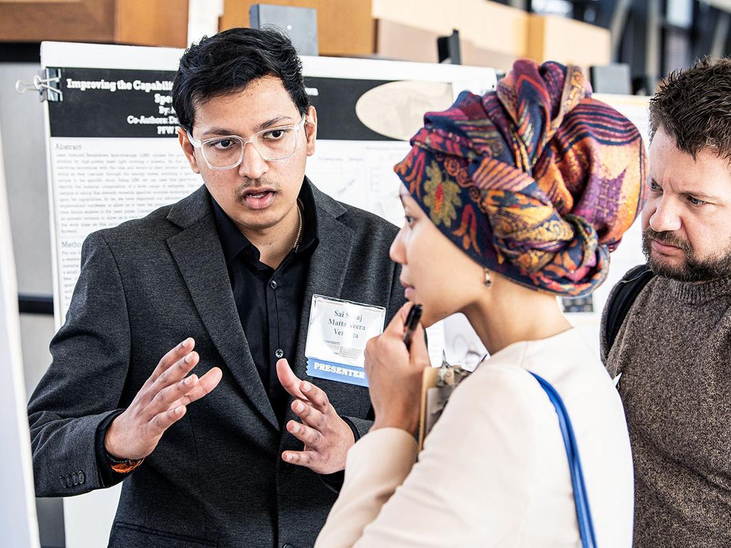 A student explains his research project to a judge at the symposium