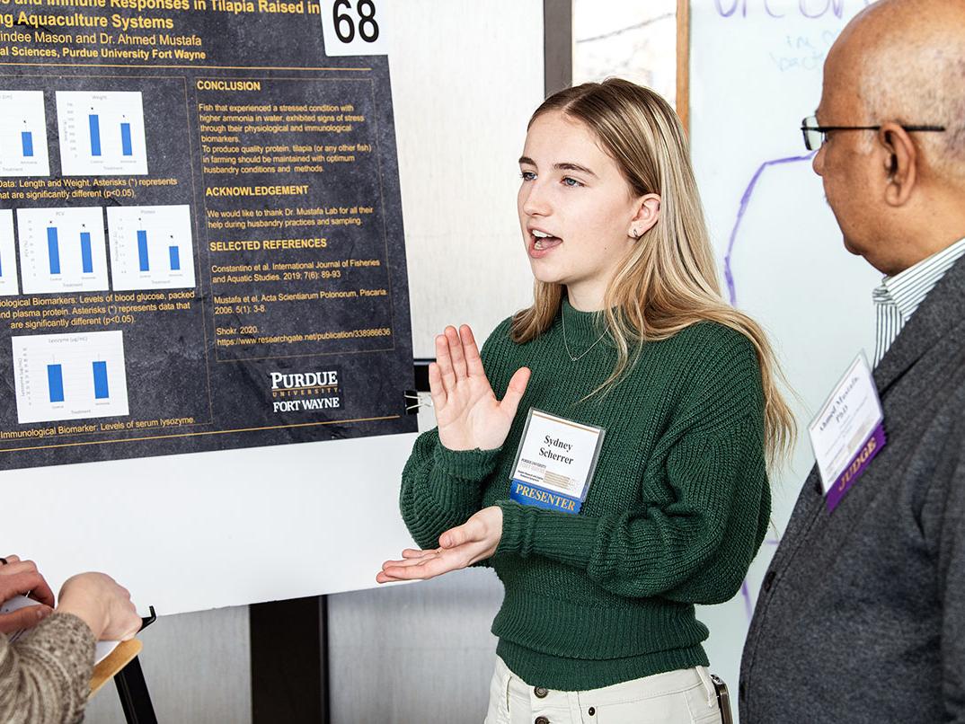 A student explains her research project to a judge at the symposium