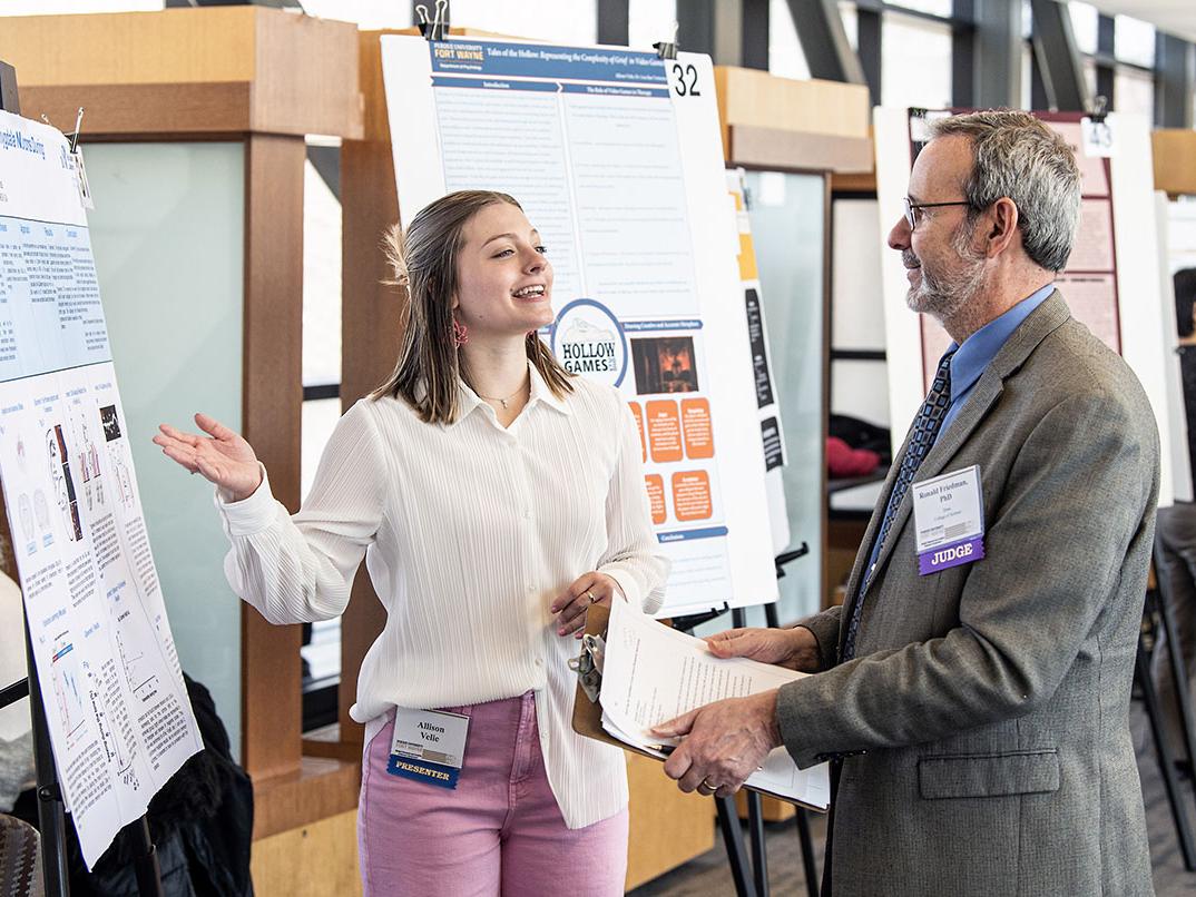 A student explains her research project to a judge at the symposium