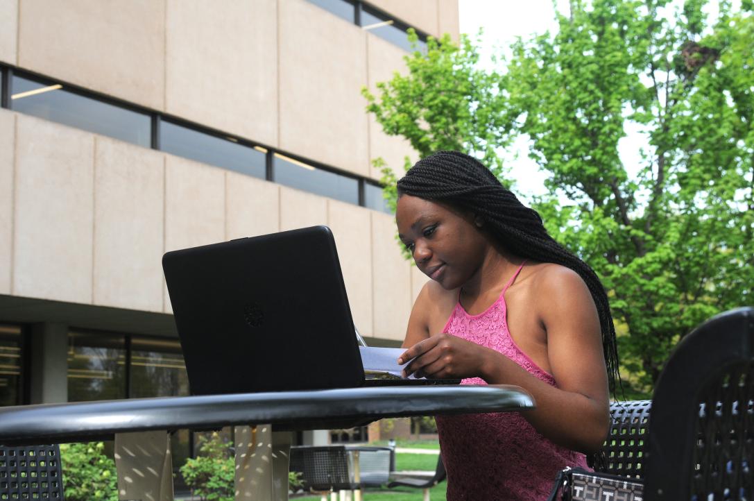 Student reads an assignment on a laptop outside.