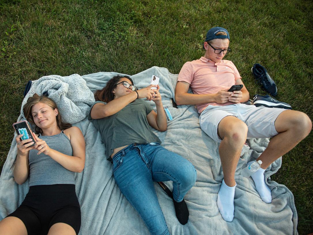 Students on the lawn read Don Life newsletter on their phones.