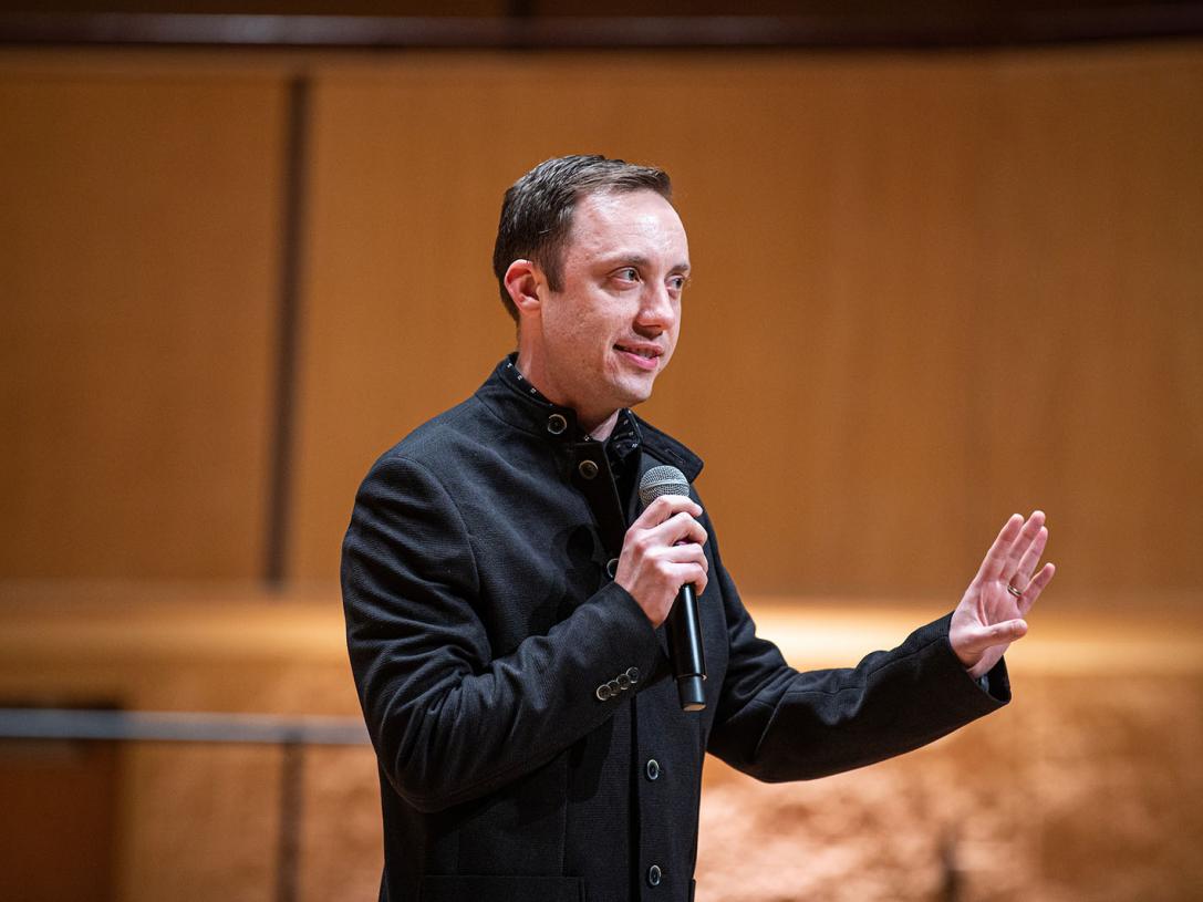 William Sauerland is onstage and speaking with a microphone