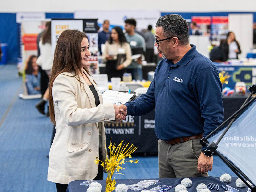 A student is shaking hands with a prospective employer at a career fair