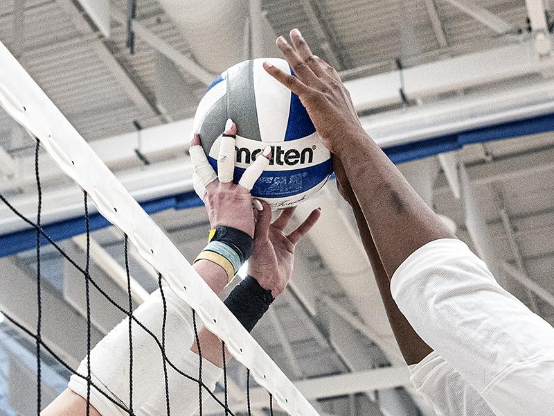 Two volleyball players are reaching for a volleyball