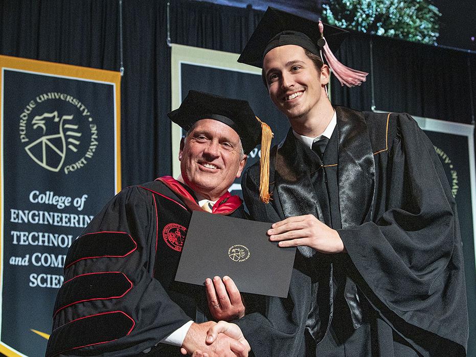 Dean John O'Connell is presenting a diploma at PFW's commencement