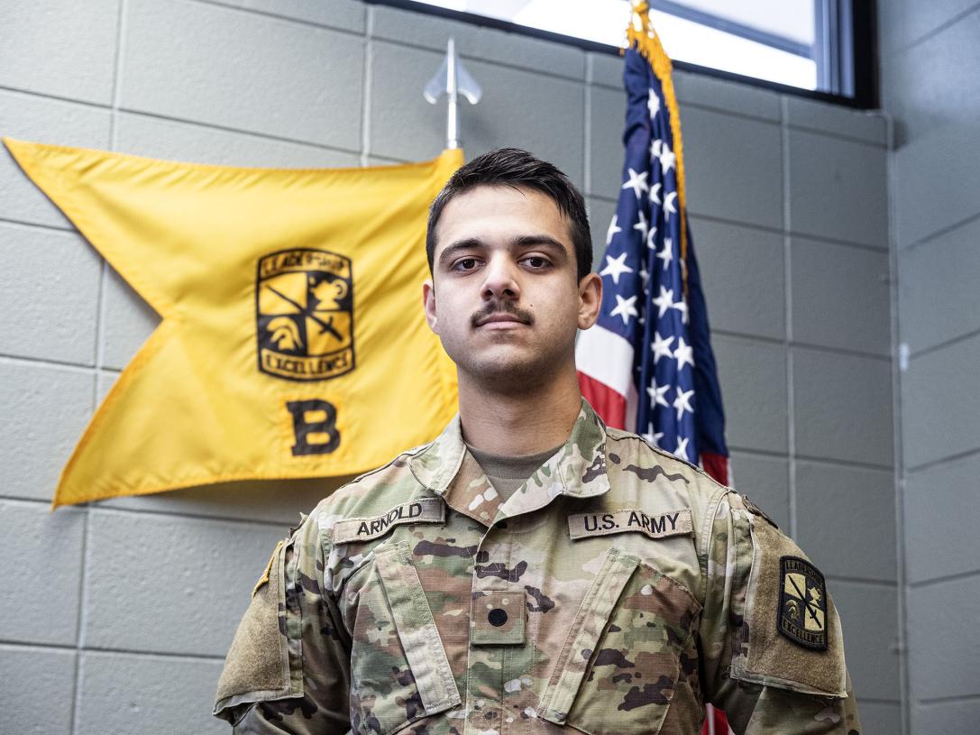Tanis Arnold is wearing an Army uniform and standing in front of two flags