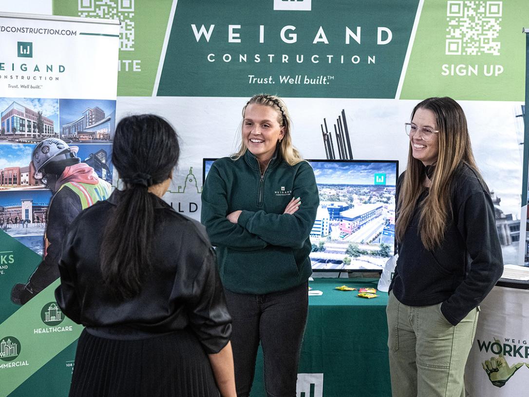 Two representatives of construction companies are speaking to a conference attendee