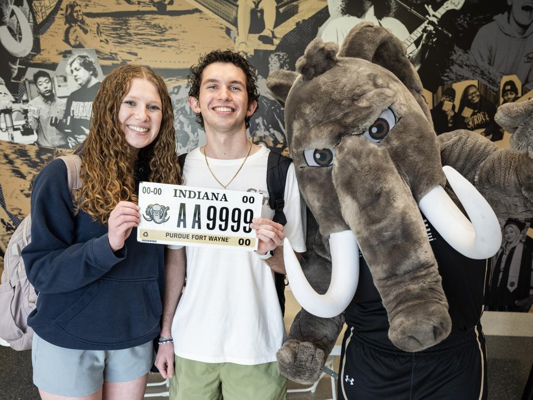 Two students pose with Don to show off a PFW license plate