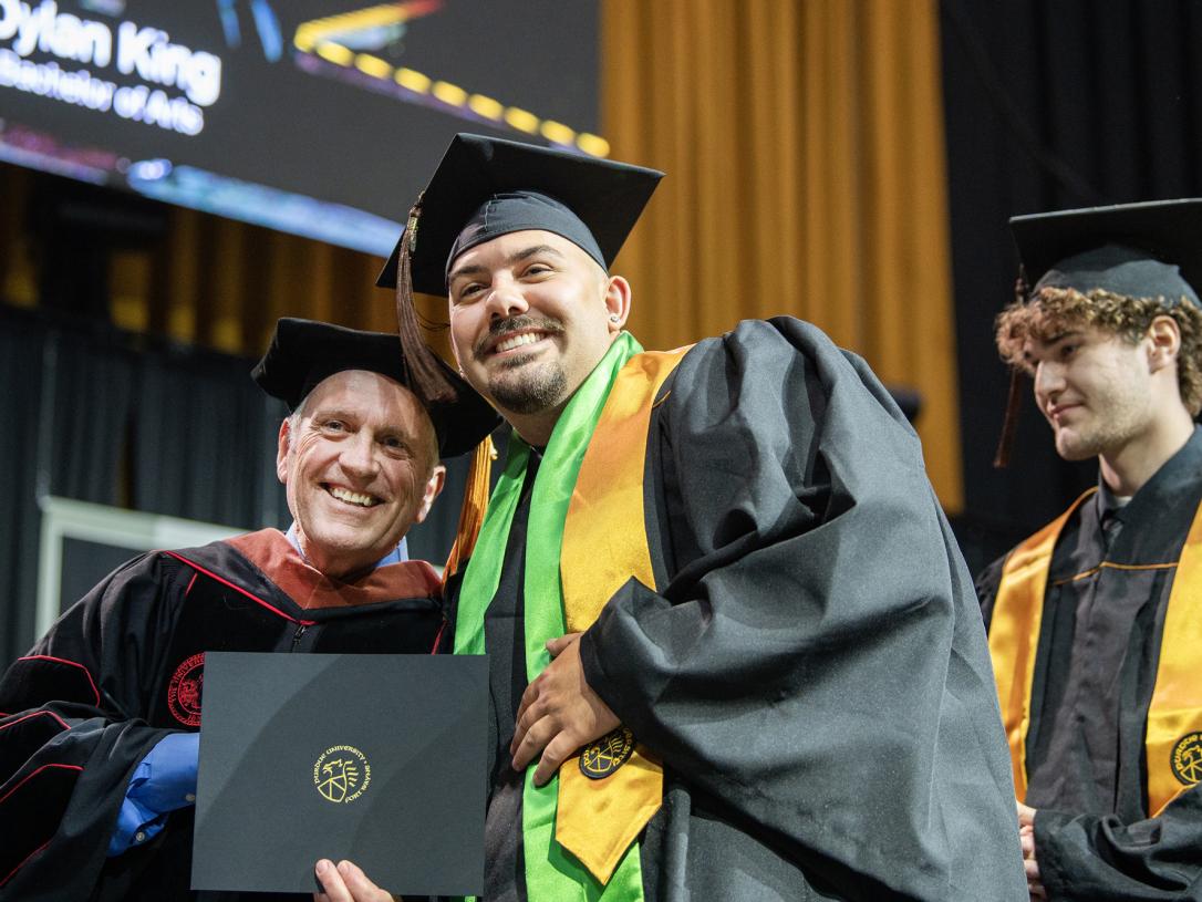 A student and faculty member pose with a degree at the 2026 commencement ceremony