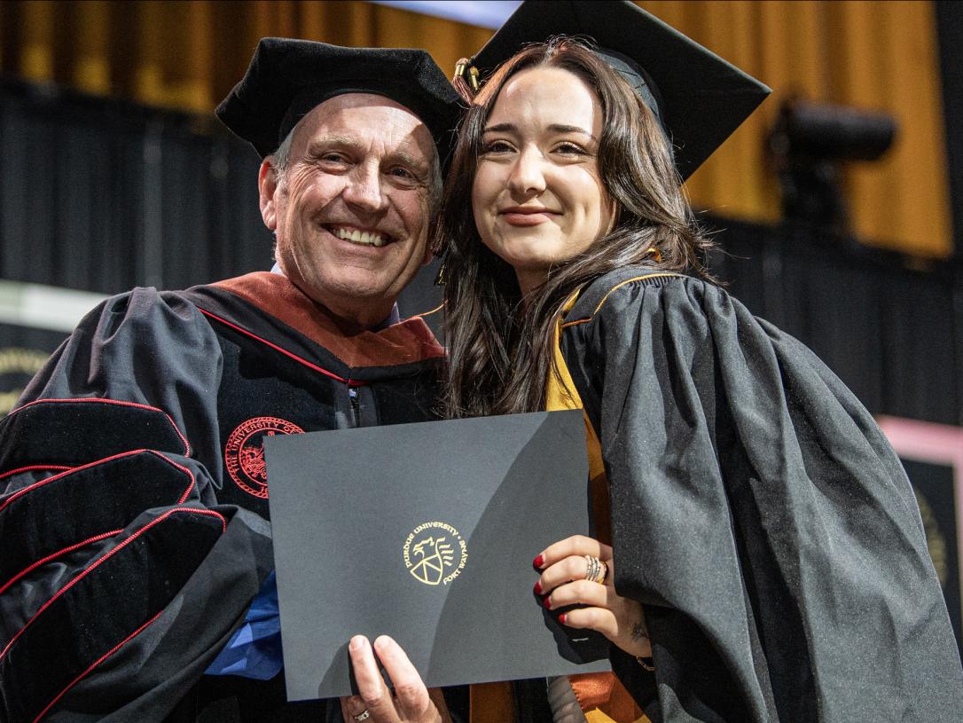 A female student and faculty member pose with a degree at the 2026 commencement ceremony