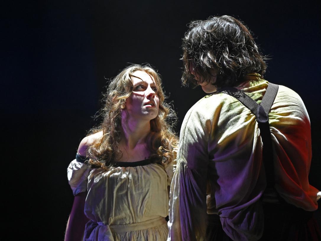 actors in dramatic lighting facing each other, we see a woman's face and the back of a man's head