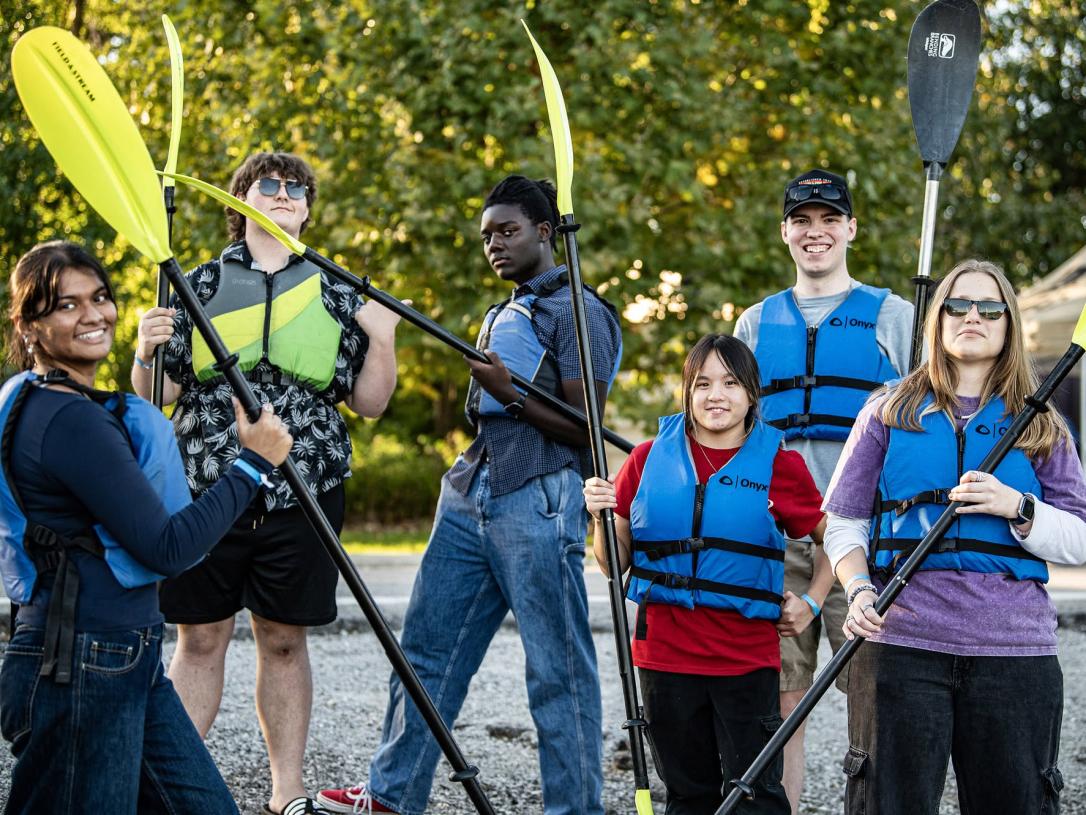 Several students are holding kayak paddles