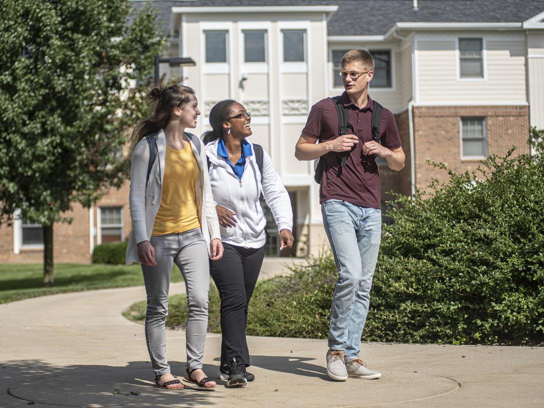 PFW students conversing while walking on the student housing campus sidewalk.