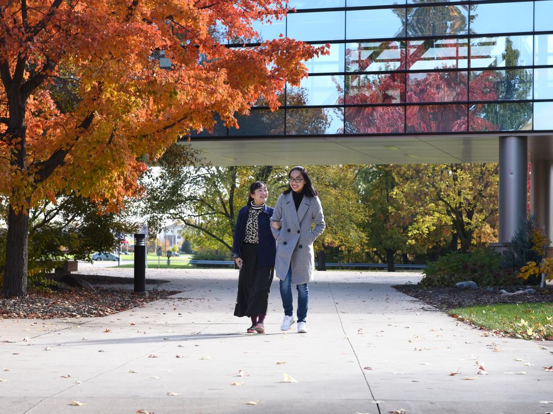 Two students walking on campus on an autumn afternoon.